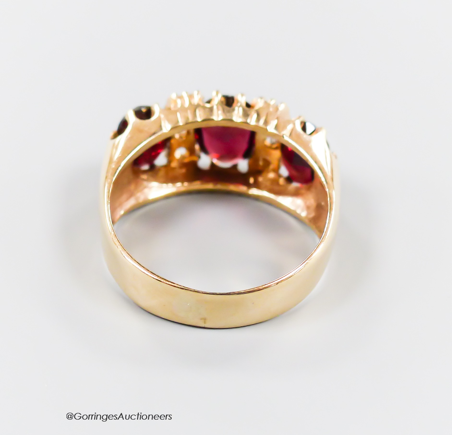 A modern 9ct gold and graduated three stone garnet set half hoop dress ring, with diamond chip spacers, size N, gross 4.9 grams.
